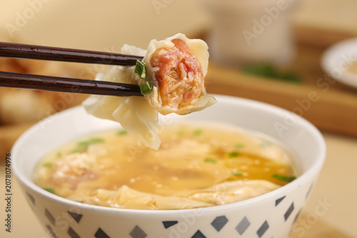 Handmade dumpling with mixed filling wrapped in dough held by chopsticks over hot soup bowl