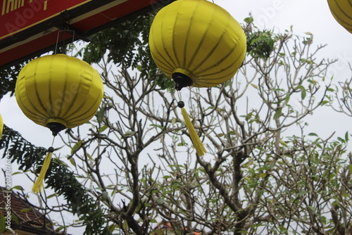 Bright yellow silk lanterns hanging from wooden frame against cloudy sky background.