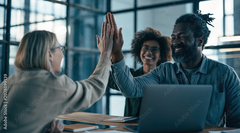 Obraz premium Happy diverse coworkers high-fiving at office with laptop