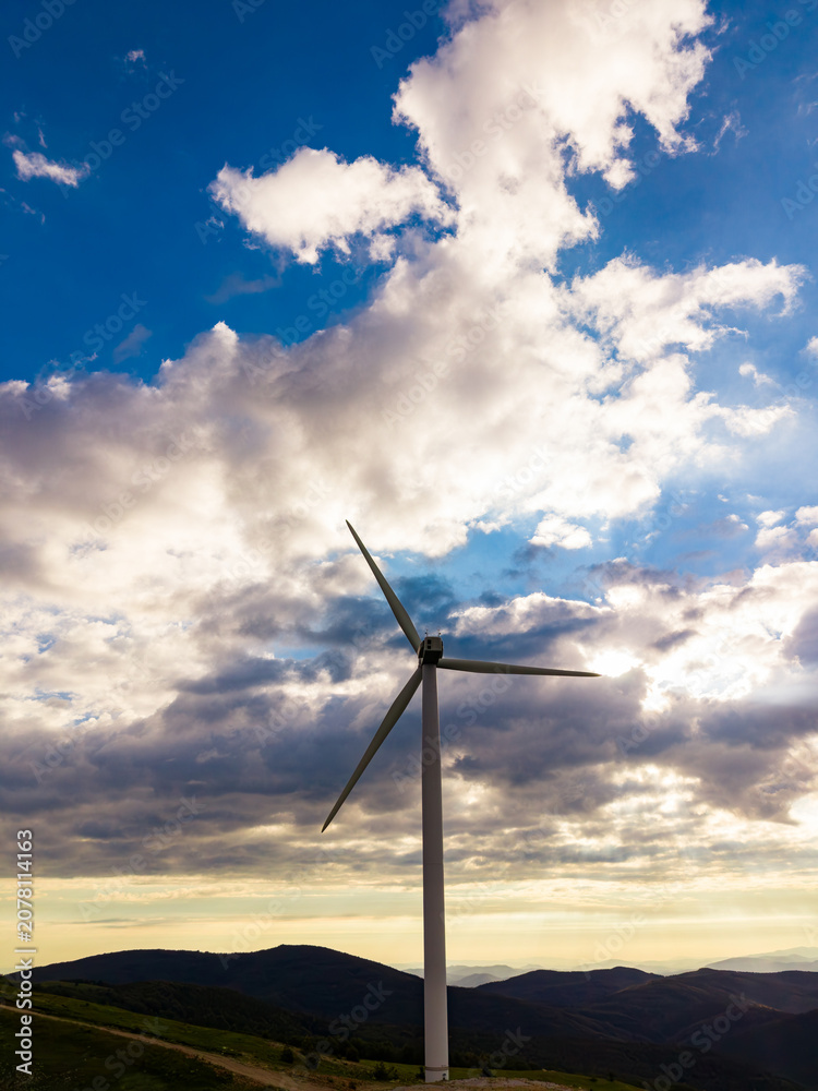 Obraz premium Wind turbine stands on a hill under a wide sky with clouds during the late afternoon