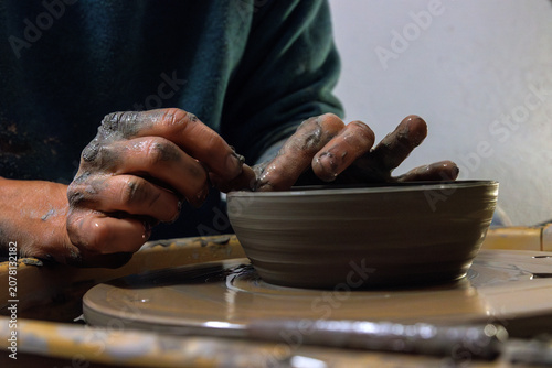 Clay covered hands shaping wet clay on a spinning pottery wheel in a ceramic studio. Selective focus. Motion effect.