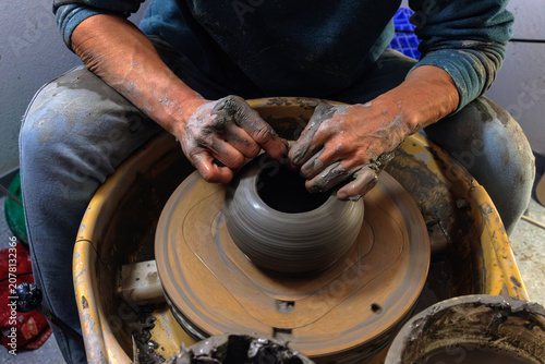 Clay covered hands shaping wet clay on a spinning pottery wheel in a ceramic studio. Selective focus. Motion effect.