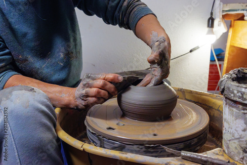 Clay covered hands shaping wet clay on a spinning pottery wheel in a ceramic studio. Selective focus. Motion effect.