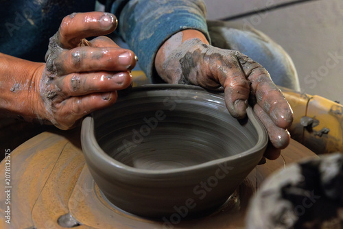 Clay covered hands shaping wet clay on a spinning pottery wheel in a ceramic studio. Selective focus. Motion effect.