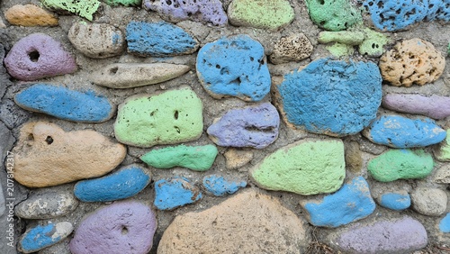 Photos A rustic stone wall featuring irregular, porous rocks painted in vibrant shades of blue, green, purple, and tan