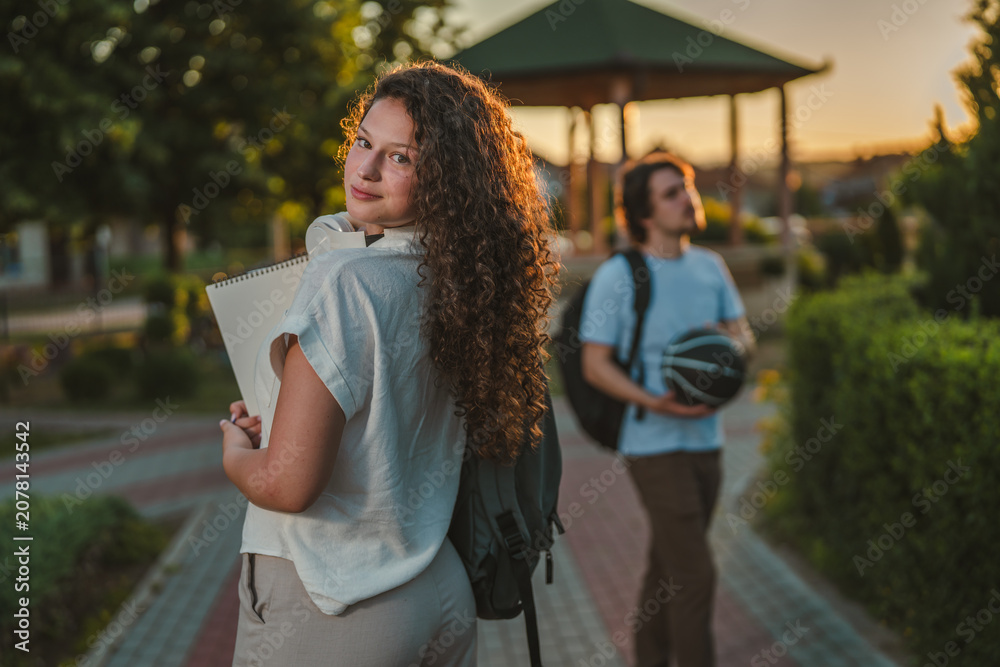 Fototapeta premium Female student looking back with male friend walking behind