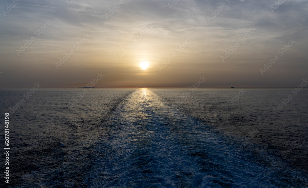 Obraz premium Sunset over calm sea with ship wake trail leading to horizon