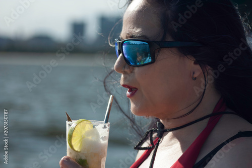 Caucasian woman enjoying a sunny day on a sailboat with sunglasses and drink with sustainable straw in Rio de Janeiro Brazil
