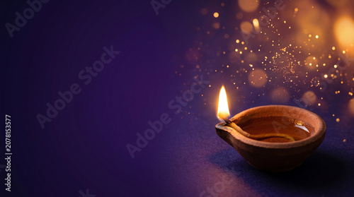 Diwali background with traditional clay diya lamp and glowing bokeh sparkles on purple backdrop