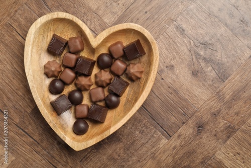 Heart shaped plate with delicious chocolate candies on wooden table, top view. Space for text