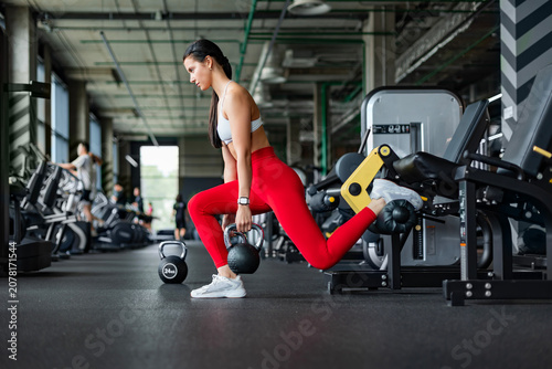 Fotografie Athletic woman doing bulgarian squats with kettlebell in gym