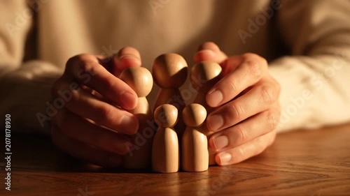 Hands protecting a group of small wooden figures on table