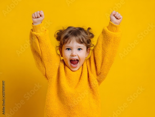 Excited child with arms raised in celebration against a vibrant yellow background.