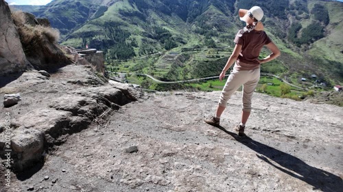 Woman standing on ancient rocks, looking out at the stunning green mountain landscape and deep valley surrounding the historic Vardzia cave monastery, exploring its medieval history in Georgia