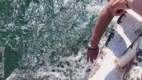 Point of view of a person's hand touching the nile river water, creating splashes and foam while sailing on a boat near philae