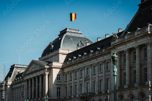 Grand neoclassical architecture facade of the Royal Palace of Brussels with the Belgian national flag flying under a clear blue sky
