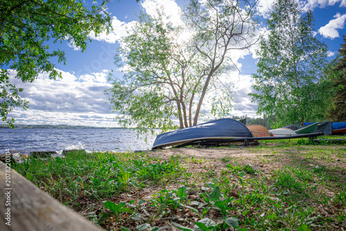Bilde på lerret A serene view of a Finnish lake shore, featuring several rowboats stored upside down on the grassy bank