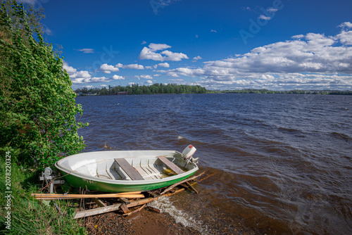 Slika na platnu A serene view of a Finnish lake shore, featuring one rowboat stored upside down on the grassy bank