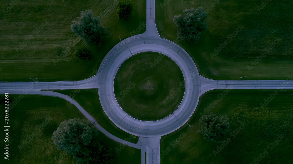 Naklejka premium Aerial view of a modern roundabout surrounded by lush greenery, highlighting its geometric design and smooth traffic flow.