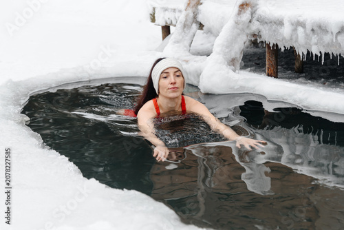 Schilderij op canvas young caucasian woman in red body swimmng in ice hole in cold water in winter, h