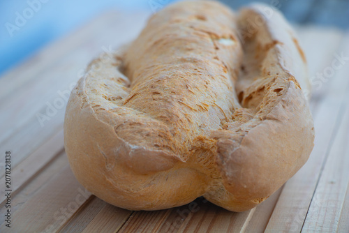 Freshly baked rustic bread loaf placed on a wooden table with a shallow depth of field. Traditional bakery product featuring a golden crust,