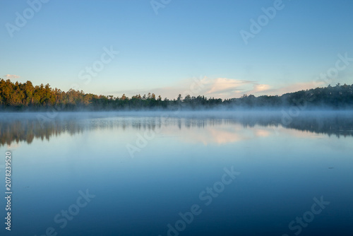 Morning fog on a blue northern Minnesota lake with pines on the shore under blue sky