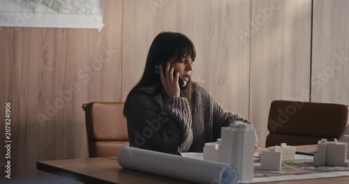 In an office, a woman talks on the phone, taking notes and focusing on an important discussion about work