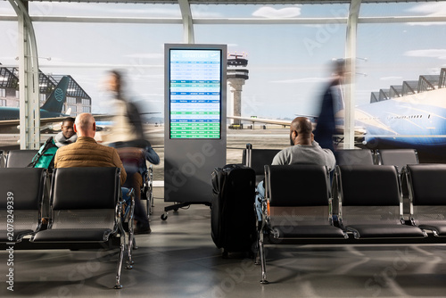 Obraz na plátne Walking, electronic departing board and men with women in hectic airport lobby, blurry motion, moving fast, flights schedule display and passengers in air transportation hub, for air travel concepts