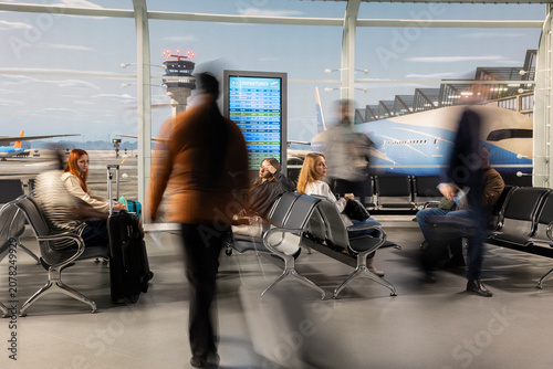 Foto Blurry travelers carrying luggage to airport security checkpoints to do check-in, hectic tourists pulling trolleys creating long exposure movement blur while walking to boarding gate