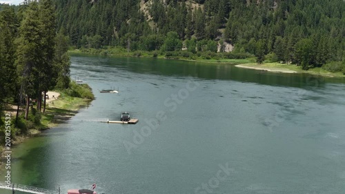 Aerial of Pend Oreille river flowing through dense forest in eastern Washington with multiple docks and boats visible along the heavily wooded shoreline