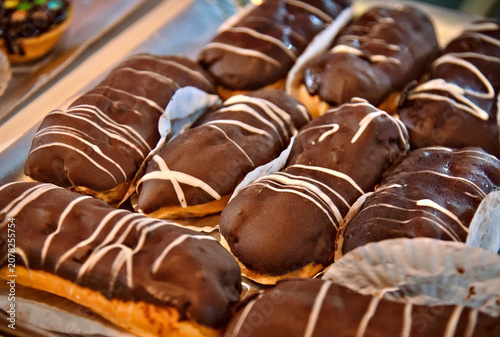 Freshly baked chocolate eclairs with white icing drizzle on display in a bakery