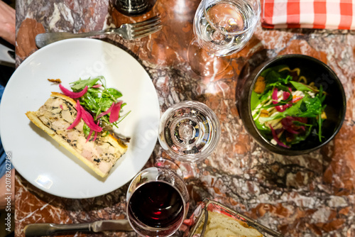 A slice of artisanal Pâté en Croûte and a skate wing ceviche salad served with red wine on a marble table at a traditional Lyonnaise bouchon. This top-down overhead flat lay captures the gourmet Frenc