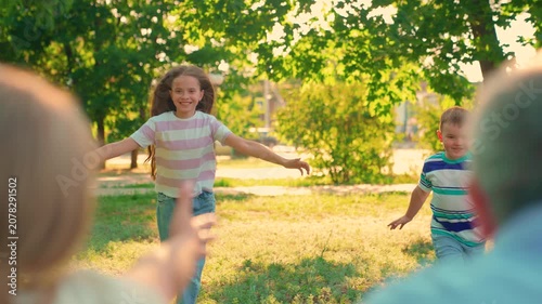 Children play run in park, hugging their parents. Family weekend. Happy family. Parents fun, mother father, kids son daughter picnic on lawn. Young boy girl hug their parents outdoors. Happy people