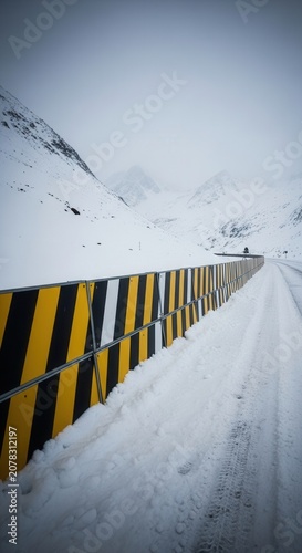 Winter Highway: Snow-Covered Road and Barrier Leading Towards the Distant Mountains Landscape