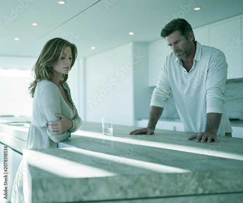 Tense couple facing emotional conflict across kitchen counter in bright modern home