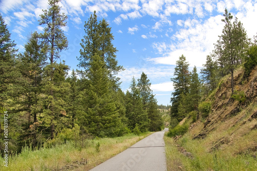 Sunny summer day view of the Trail of the Coeur d’Alenes beside a rocky hill in the forest near Plummer, Idaho.