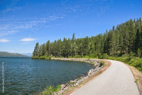 Sunny summer day view of the Trail of the Coeur d’Alenes winding along the lakeshore in the forest near Harrison, Idaho.