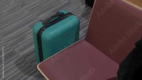 Teal hard shell suitcase standing beside waiting seat at airport terminal