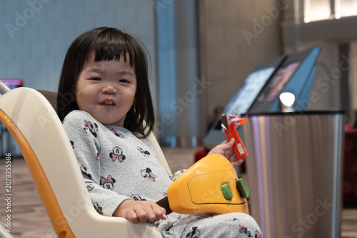 Fotografía A close-up portrait of a smiling young girl sitting in a child safety seat attached to an airport trolley at Airport