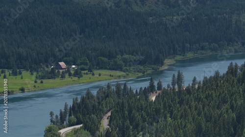 Aerial of Pend Oreille river in forested valley in Ruby Washington in summer with open grassy areas and rural buildings