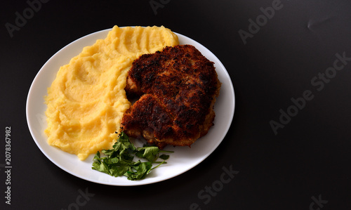 A pork chop fried in breadcrumbs with mashed potatoes on a round plate against a black background.