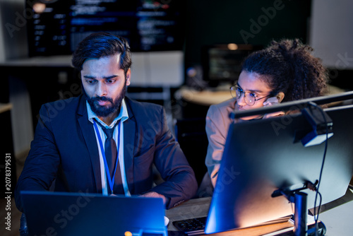 Bild auf Leinwand An analyst manipulates data on a futuristic touchscreen showing a luminous rotating sphere in a dark control room, surrounded by the soft blue light of many monitors in a professional