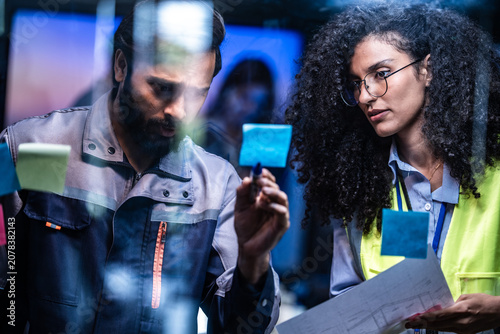 Принти на полотні Analysts collaborate across rows of glowing screens in a darkened cyber operations room during a busy shift, lit by the cool blue glow of the displays amid the soft hum of a busy operations