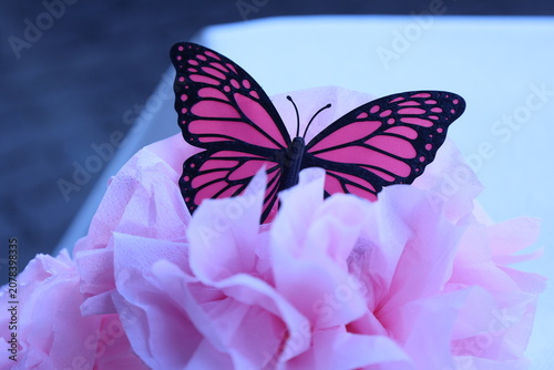 Papillon décoratif rose et noir posé sur une fleur en papier