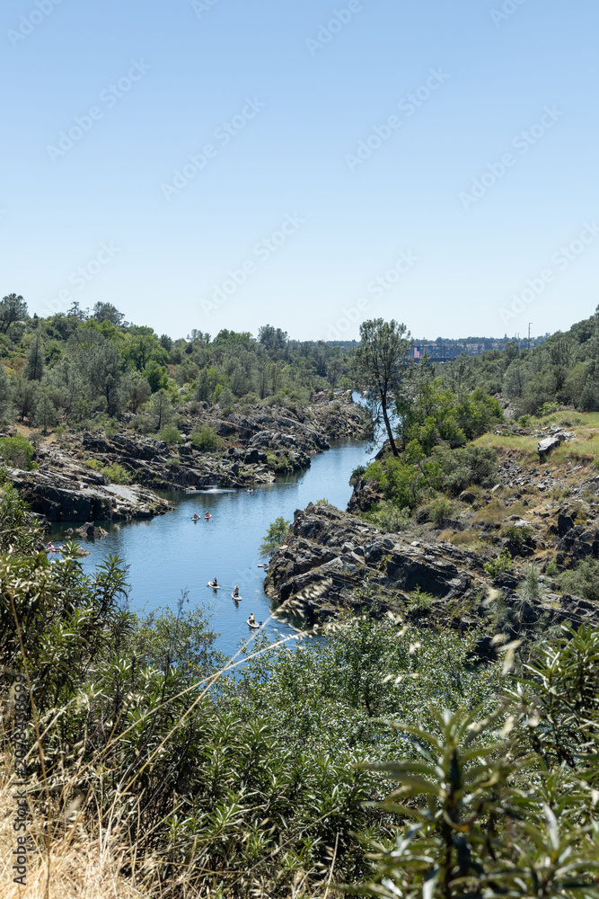 Fototapeta premium View of a river surrounded by rocks and trees with people swimming on a sunny day