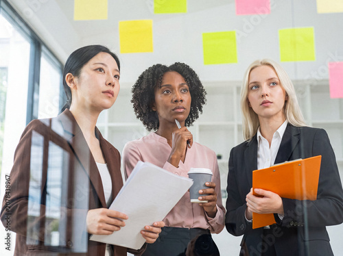 Tableau sur toile Diverse businesswomen intently analyzing colorful sticky notes on a transparent glass board in a contemporary office