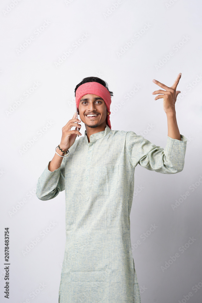Fototapeta premium happy young indian farmer using smartphone standing on white background
