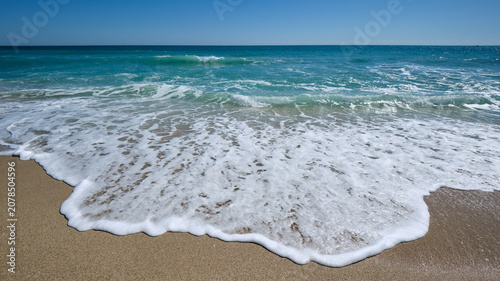 Obraz na płótnie Foamy wave washes up  from a tropical blue sea onto a sandy beach