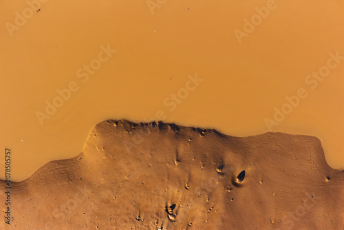 Fotografie Close-up view of alien-like clay puddle shore at a quarry with textured mud surf