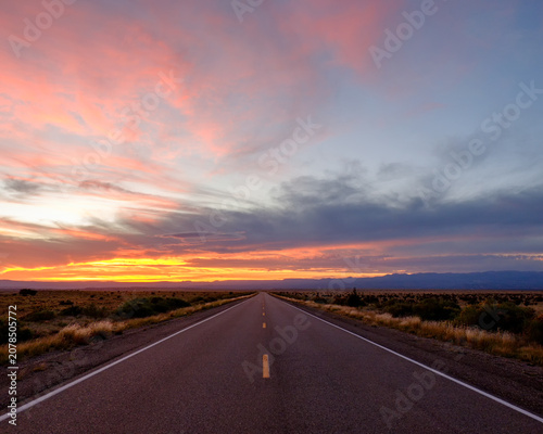 Foto Long, straight desert highway vanishing into the horizon beneath a dramatic suns